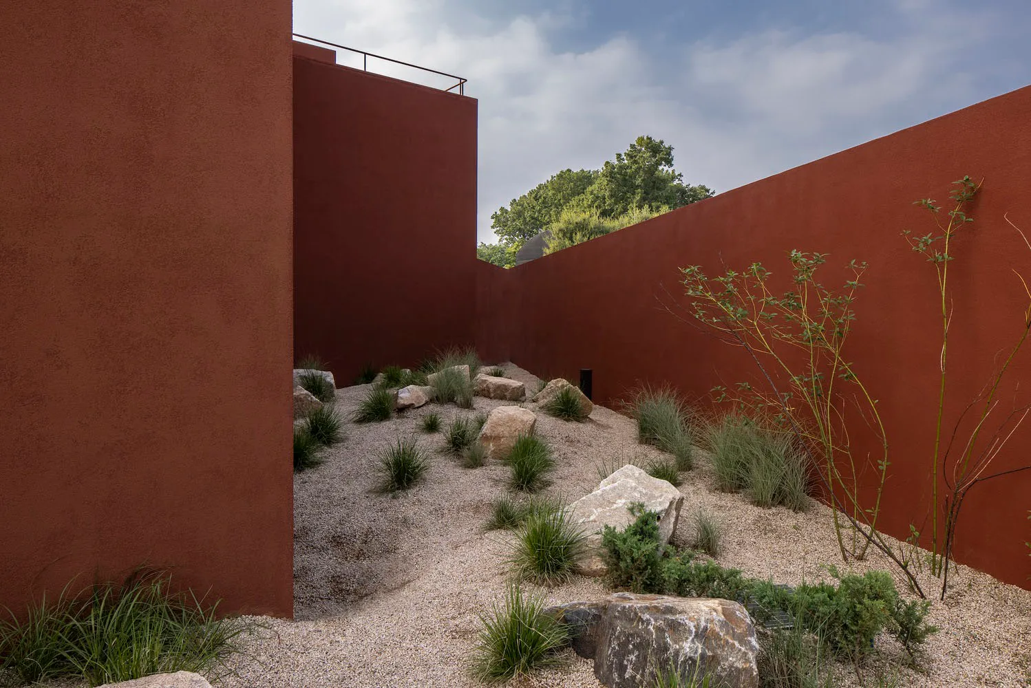 A serene outdoor courtyard with a red brick wall, stone walkway, and natural ambiance, surrounded by rocks and daylight
