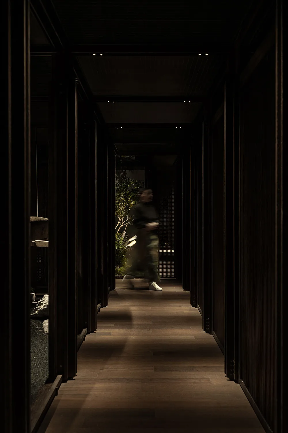 A hallway with wooden floors and walls, featuring two people walking and engaged in conversation