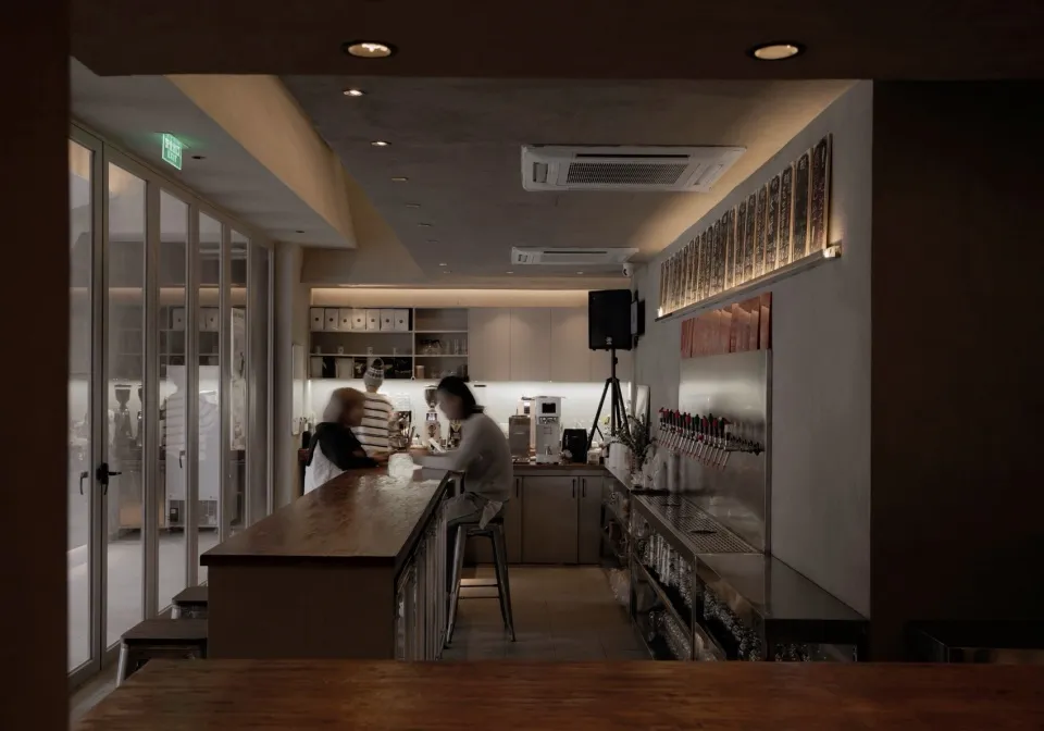 A casual restaurant bar area with patrons enjoying their time together, featuring a counter with bottles, cups, and bowls, and a refrigerator in the background