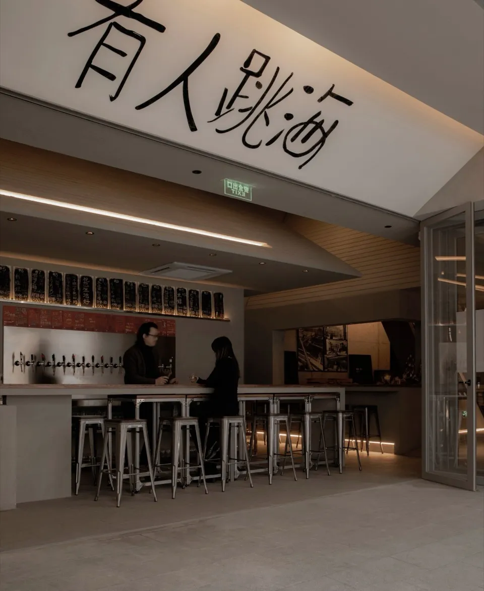 Casual modern restaurant with a bar featuring stools and tables, bottles on display, and a contemporary design