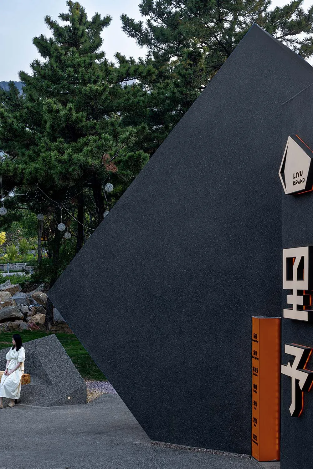 現代黑色建築，側面有大型三角形造型，兩位女性站在前方，營造寧靜而親切的氛圍
