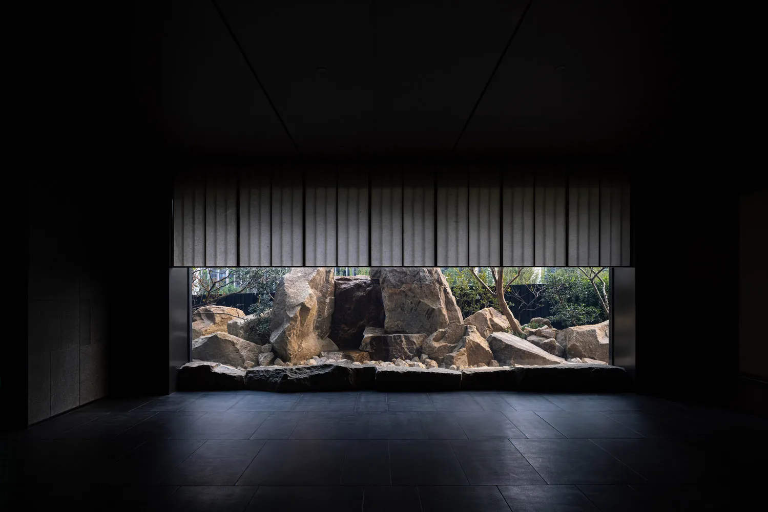 A dark and moody indoor space with a large rock wall backdrop and scattered rocks, creating a unique environment