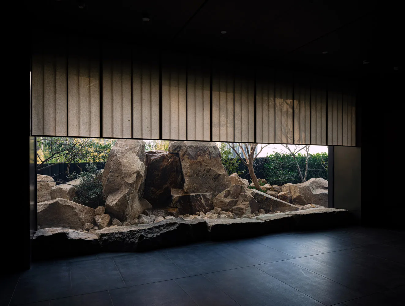 Indoor space with a rock wall and a window offering a view of the outside landscape, featuring rocks and trees