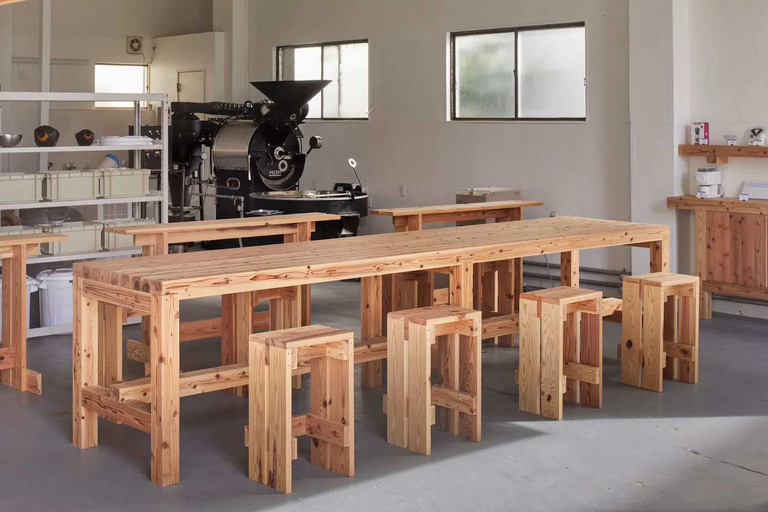 Industrial workspace with a large wooden table and chairs, well-lit with natural light or overhead lighting