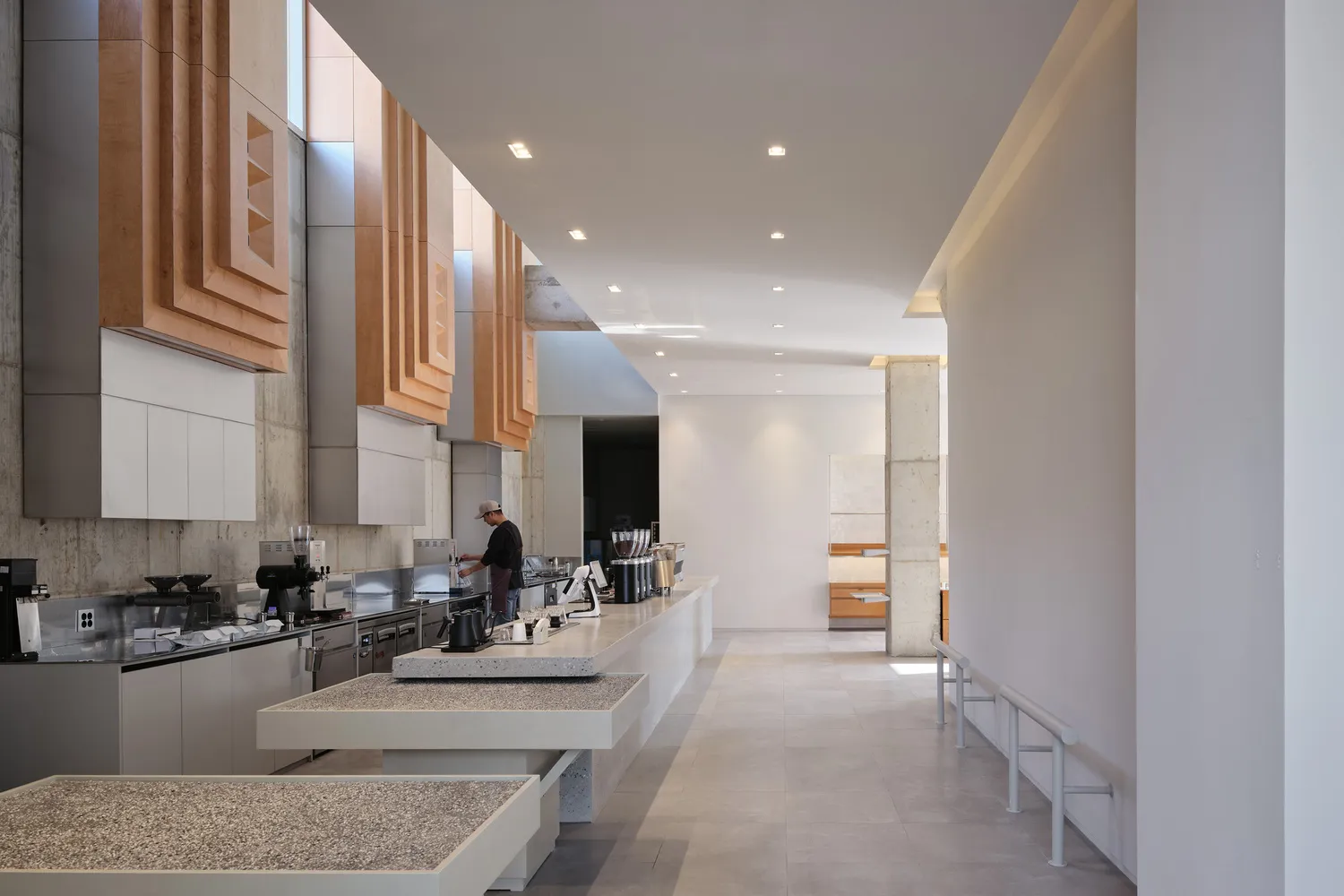 Empty restaurant kitchen with white walls and floors, featuring tables, chairs, appliances, and kitchen utensils, conveying a sense of orderliness and readiness for use