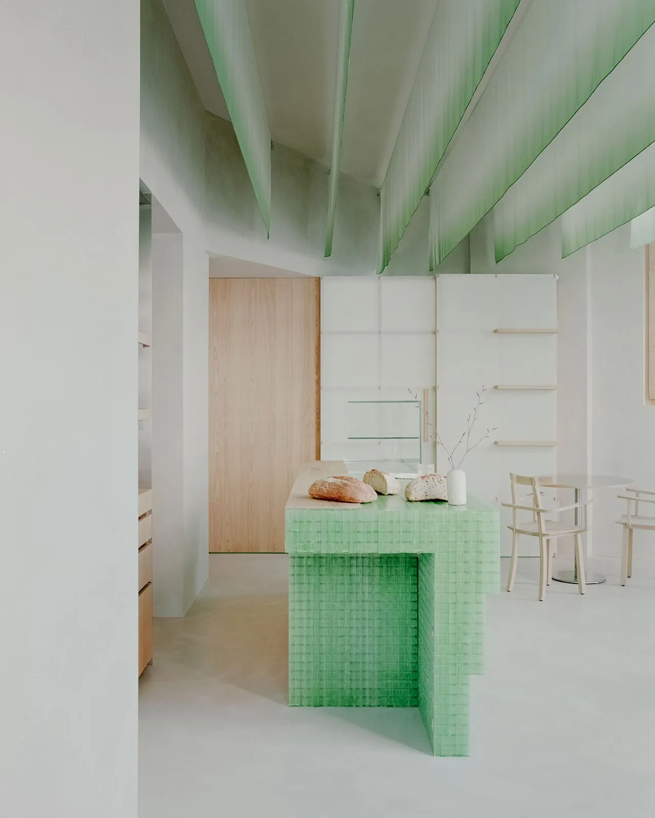 Open kitchen with green countertops, white walls, and a dining table, featuring a clean and organized atmosphere with a focus on functionality and simplicity
