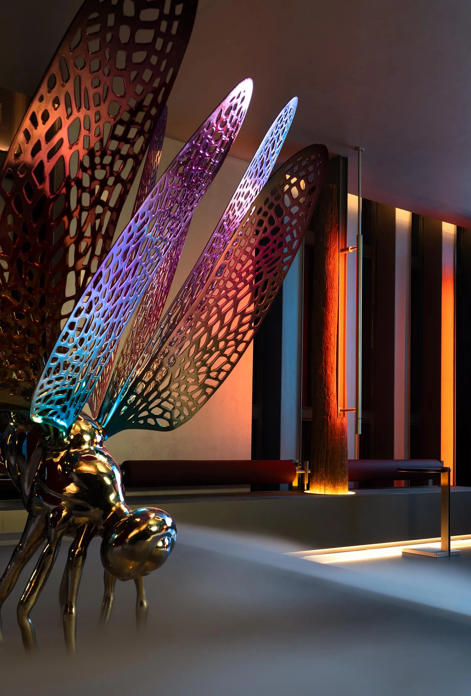 A metal sculpture of a dragon with a butterfly design sits on a table near a wall, surrounded by a chair and two benches in a contemporary setting