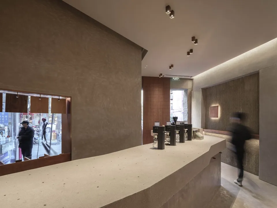 A casual cafe interior with a counter area, wooden accents, and a person walking past, serving beverages to customers