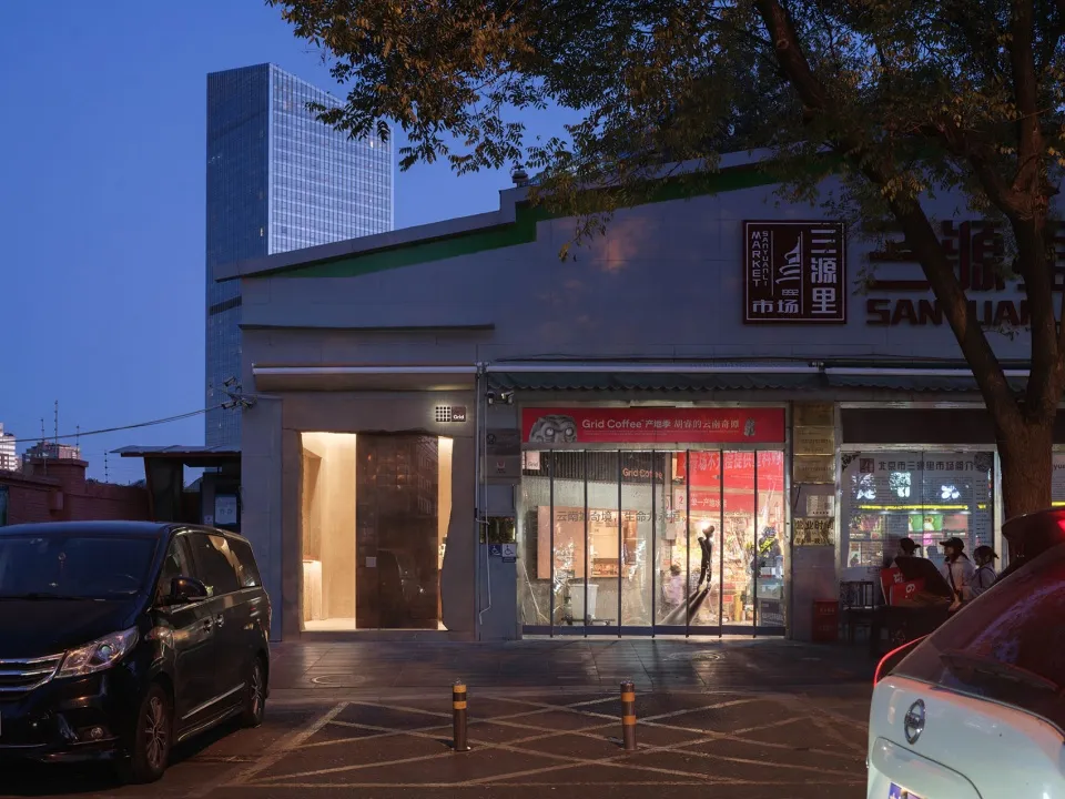 A modern Asian restaurant at night with a gray and white exterior and a cozy interior featuring dim lighting and warm tones, with chairs and dining tables for customers