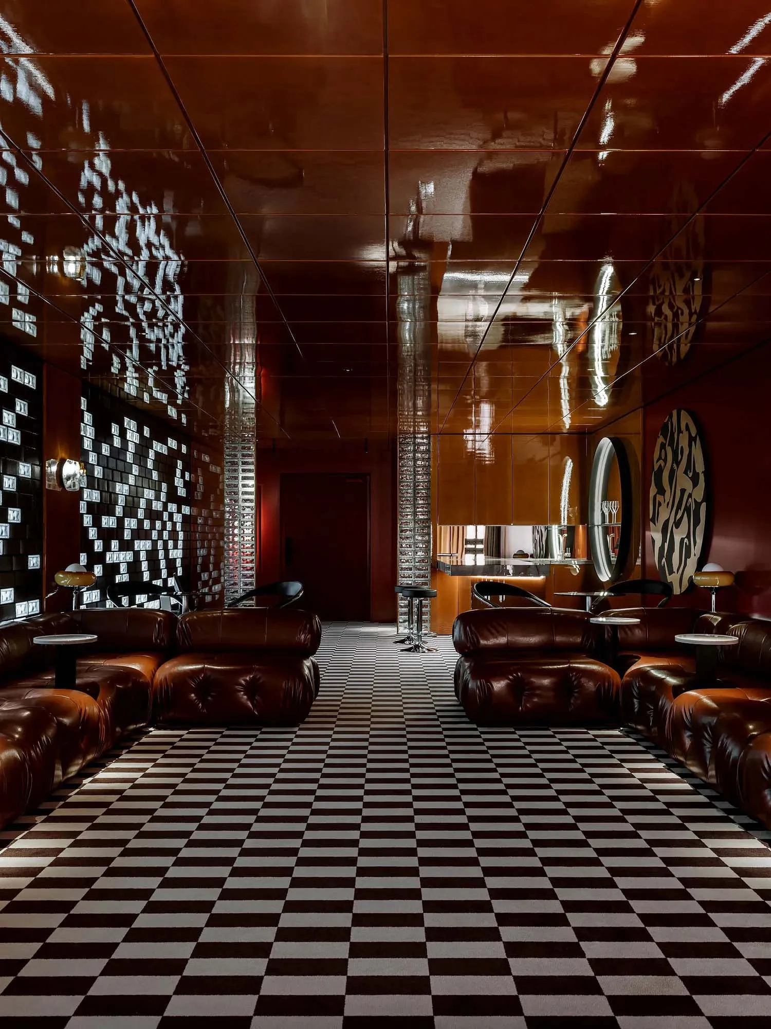 A modern living area with a checkered floor, leather chairs, and a mix of wood and metal materials, featuring warm lighting and a comfortable atmosphere