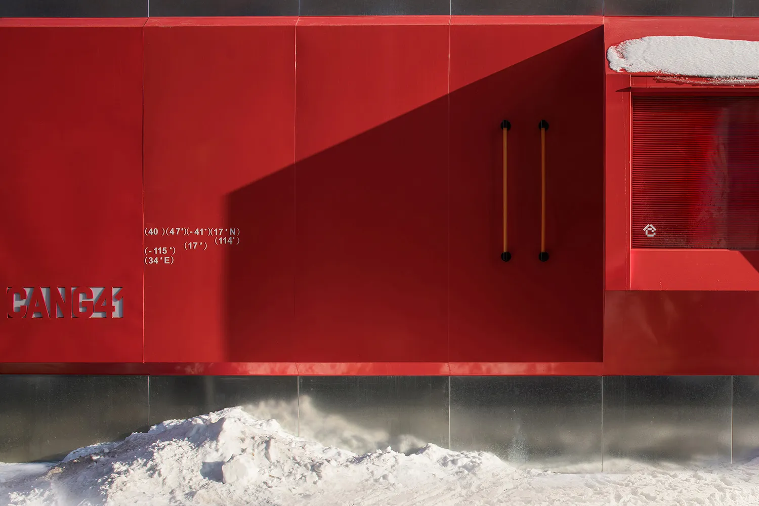 A red door with yellow handles in front of a building, set against a neutral background