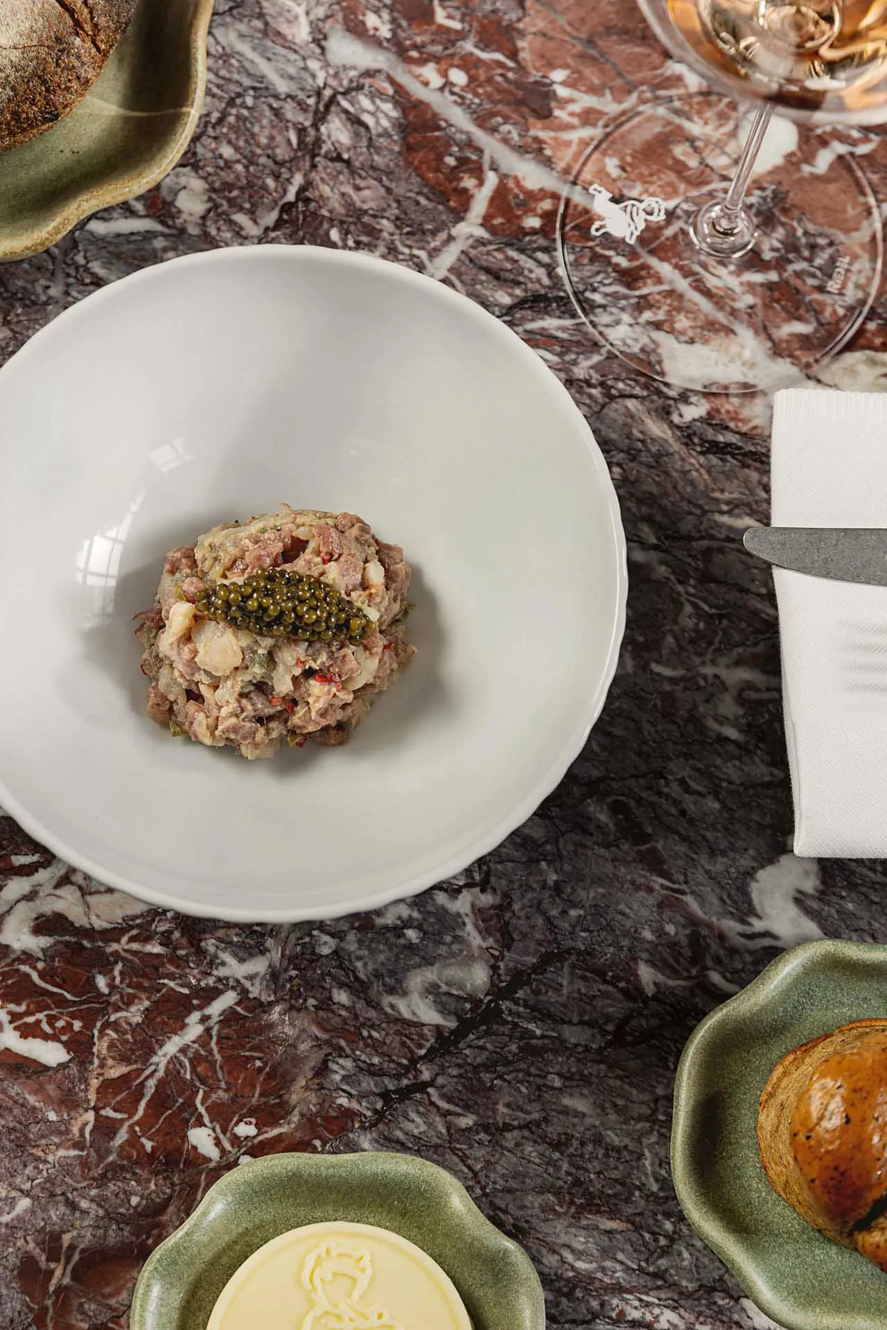 A dining table set in a restaurant with a marble countertop, a white bowl, knives, and a wine glass, creating an elegant and sophisticated atmosphere