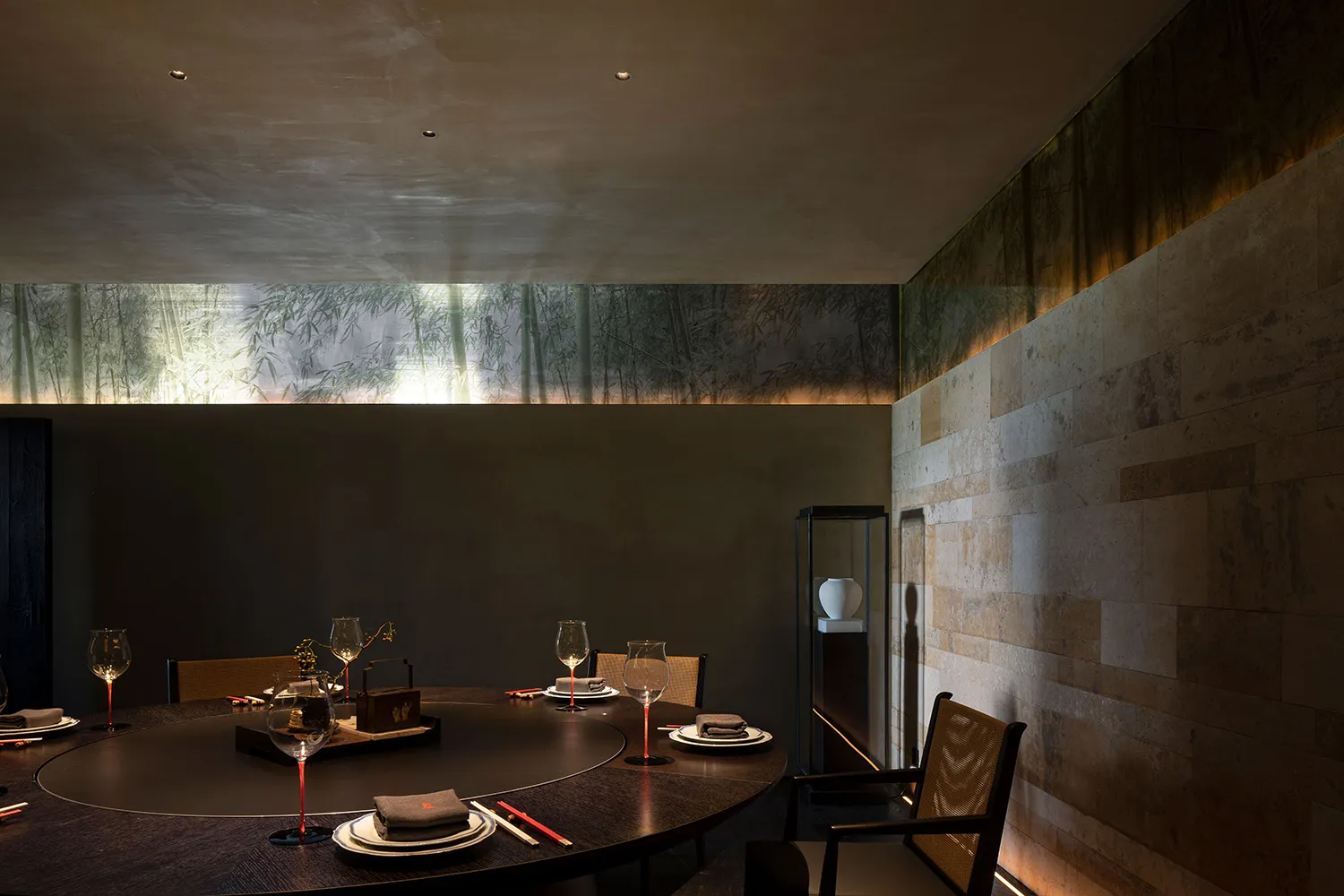 A traditional Asian dining space with a round table set for dinner, surrounded by chairs, bamboo accents, and decorative artwork