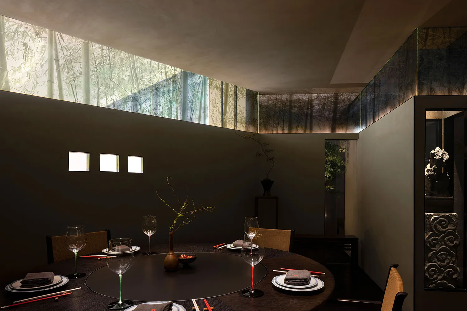 Elegant dining space with a round table, chairs, wine glasses, and bowls of food, featuring a modern design and inviting atmosphere