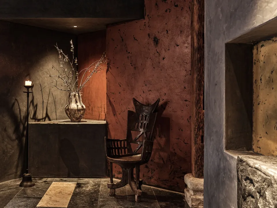 A cozy living space with a wooden chair and a vase on a table, set against a wall