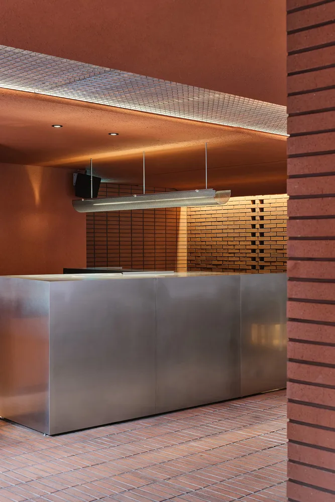Industrial kitchen with a large silver countertop, two sinks, and a hanging lamp providing illumination