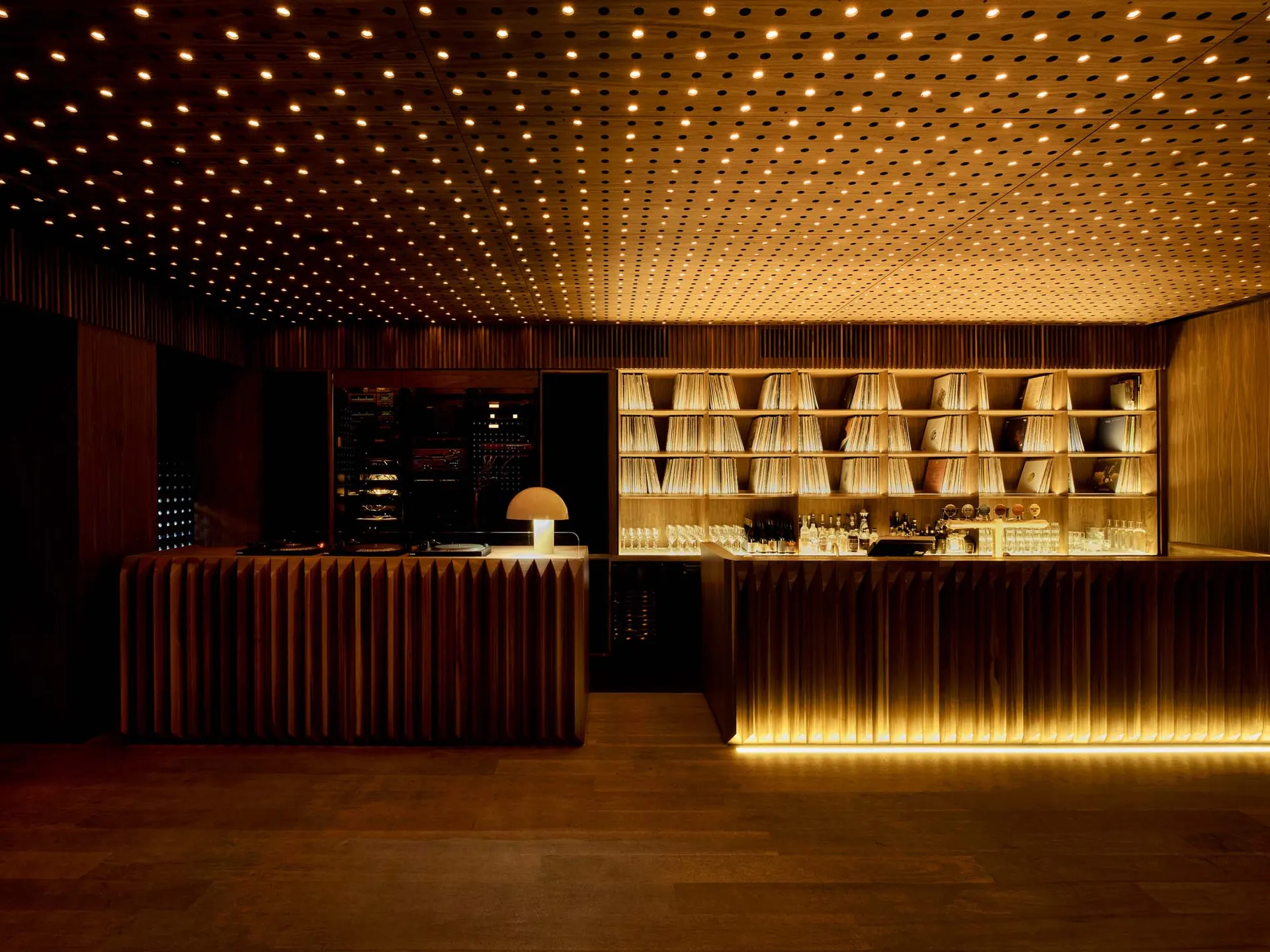 A sophisticated bar area with a long counter featuring wine glasses and bottles, surrounded by modern wood and metal elements