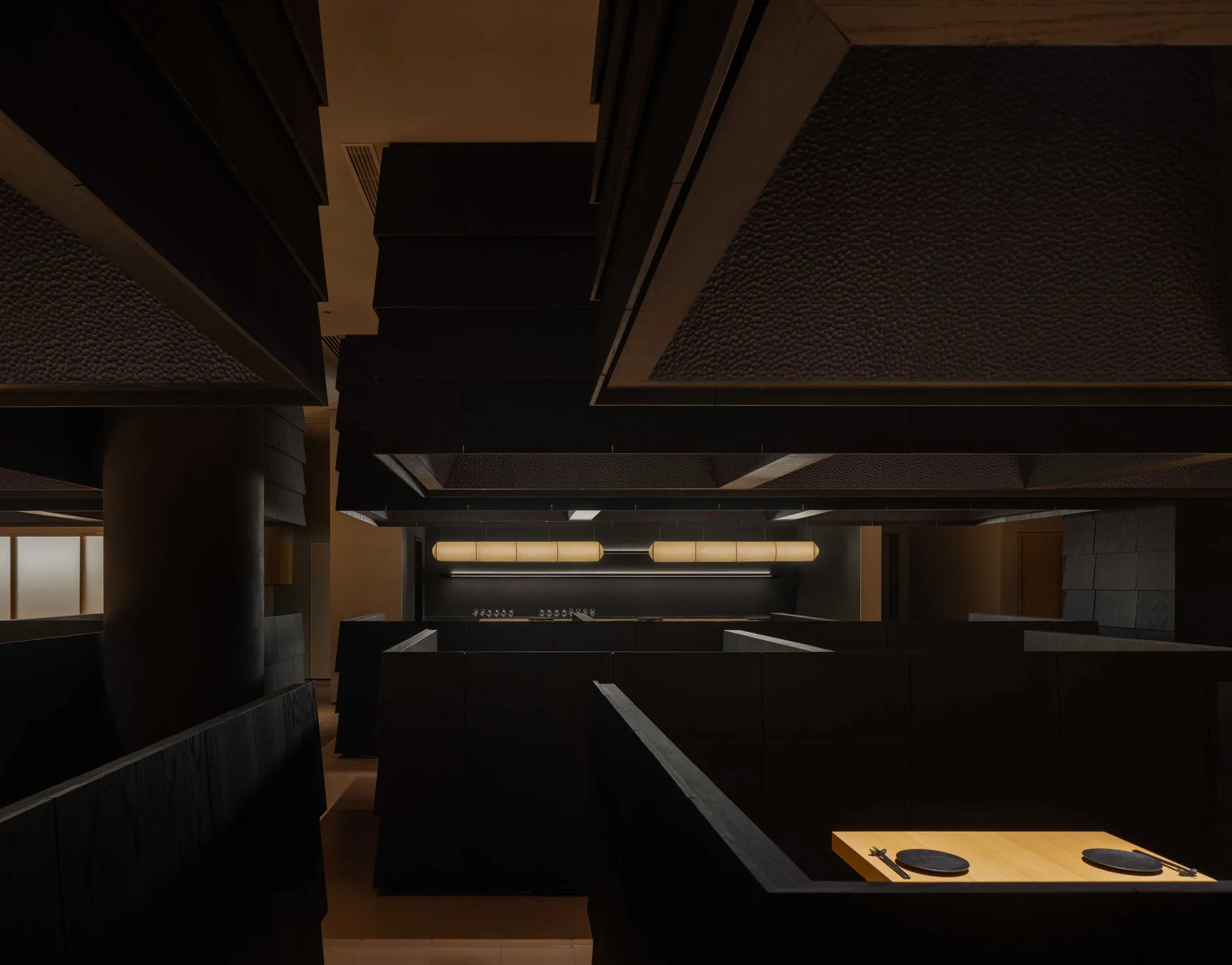 Dark restaurant kitchen with black walls and floors, featuring several tables and chairs