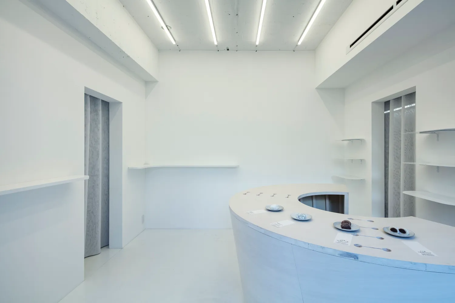 A minimalist kitchen dining space with white surfaces, a large counter, and a sink and refrigerator, giving off a clean and bright atmosphere
