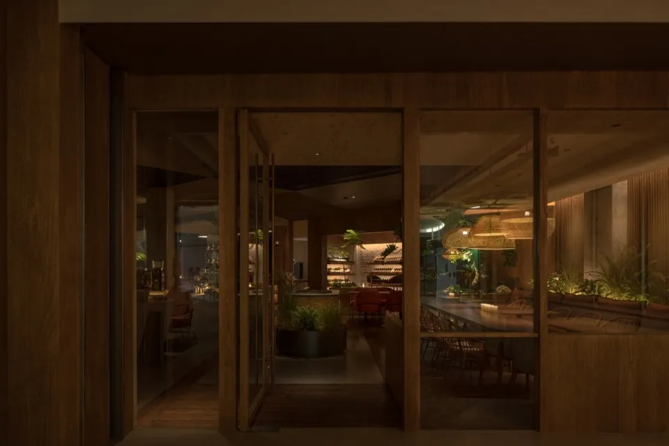 Open living area with wooden floors and walls, featuring a dining table, chairs, and a potted plant, creating a warm and inviting atmosphere