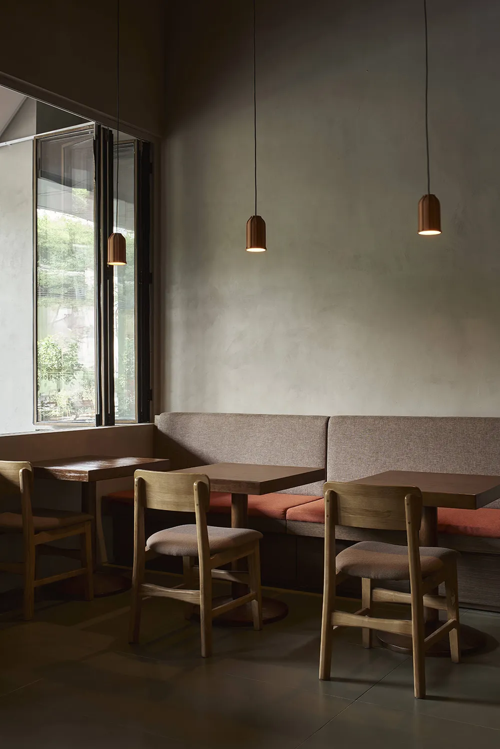 A modern restaurant interior with gray walls, dim lighting, and a cozy atmosphere, featuring a dining area with tables, chairs, and benches