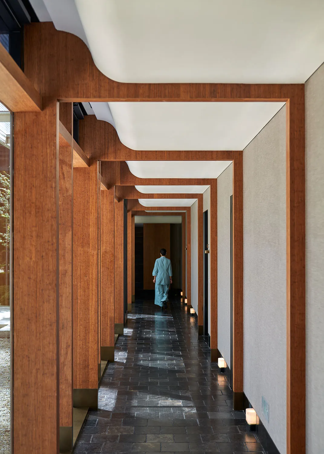 A woman walks down a traditional hallway with wooden walls and floors, surrounded by a calm and serene atmosphere