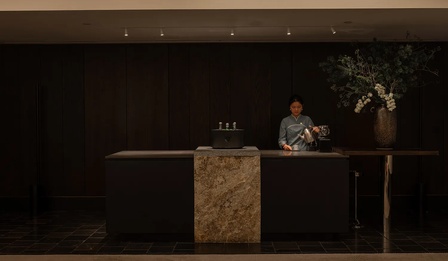 A casual cafe interior with a wooden counter, a coffee maker, and a woman standing behind it