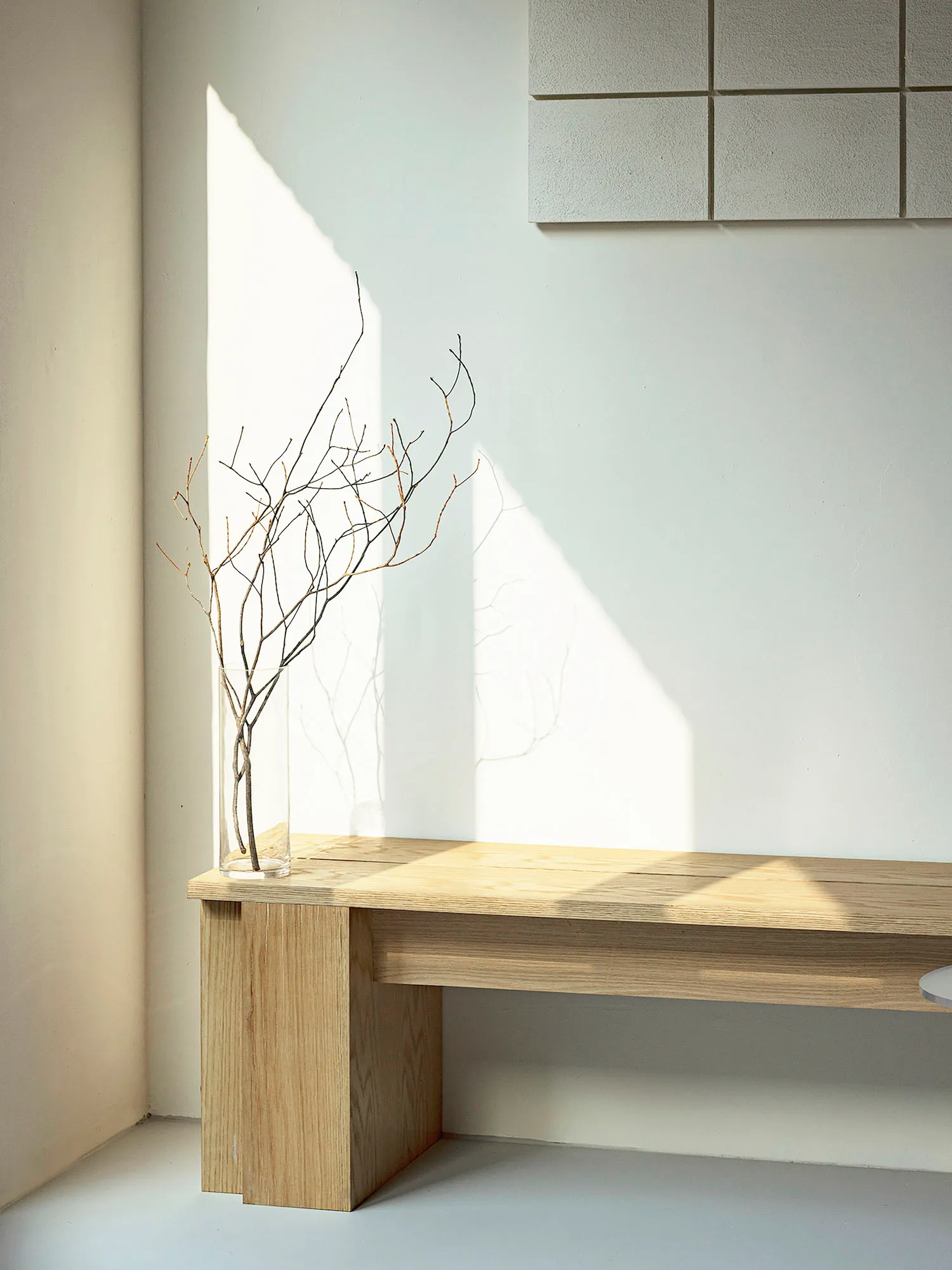 A wooden table with a vase sits in a serene indoor space surrounded by two trees and natural elements