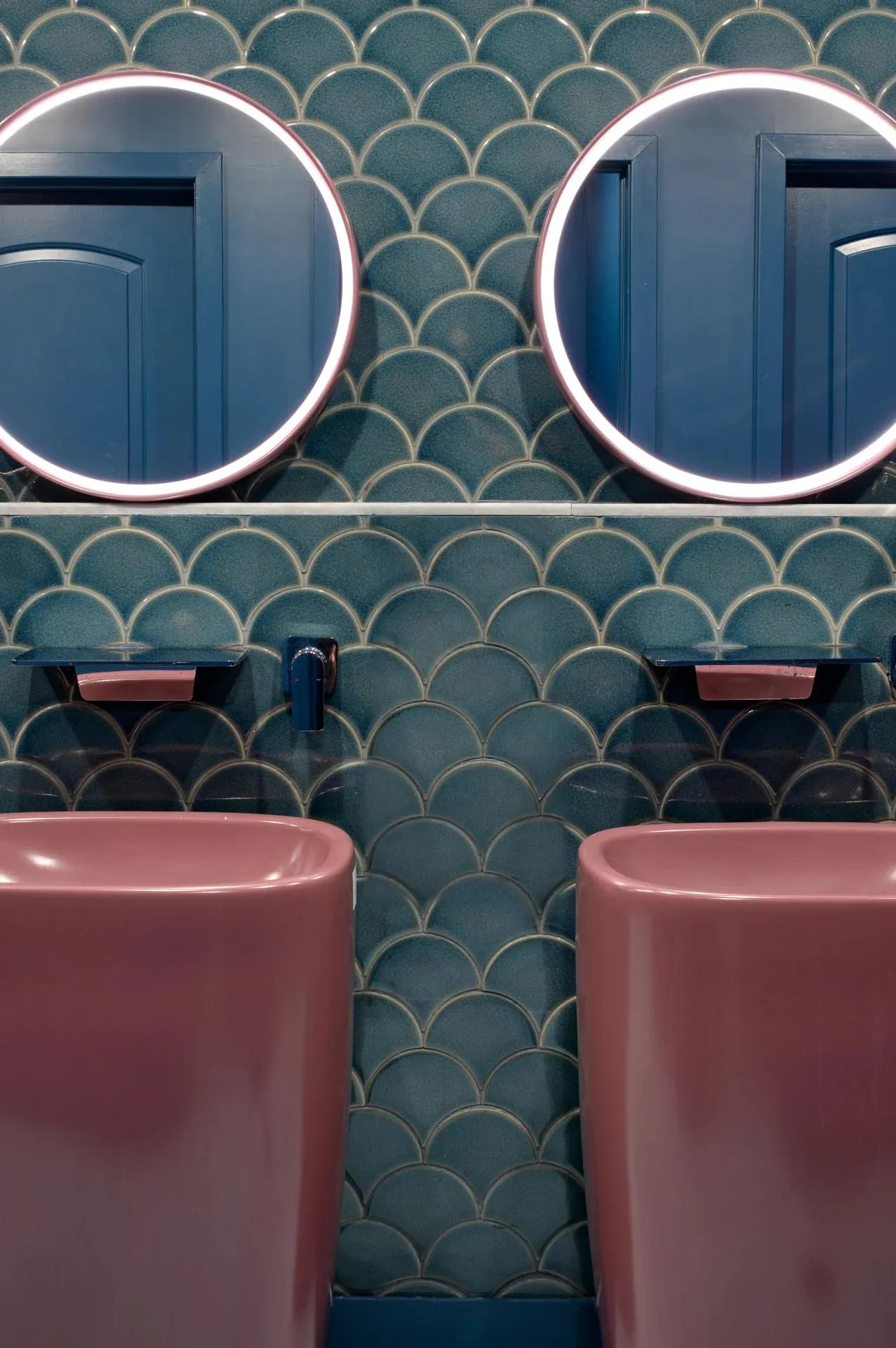 Bathroom with two pink sinks on a purple wall featuring a fish scale pattern, flanked by two mirrors