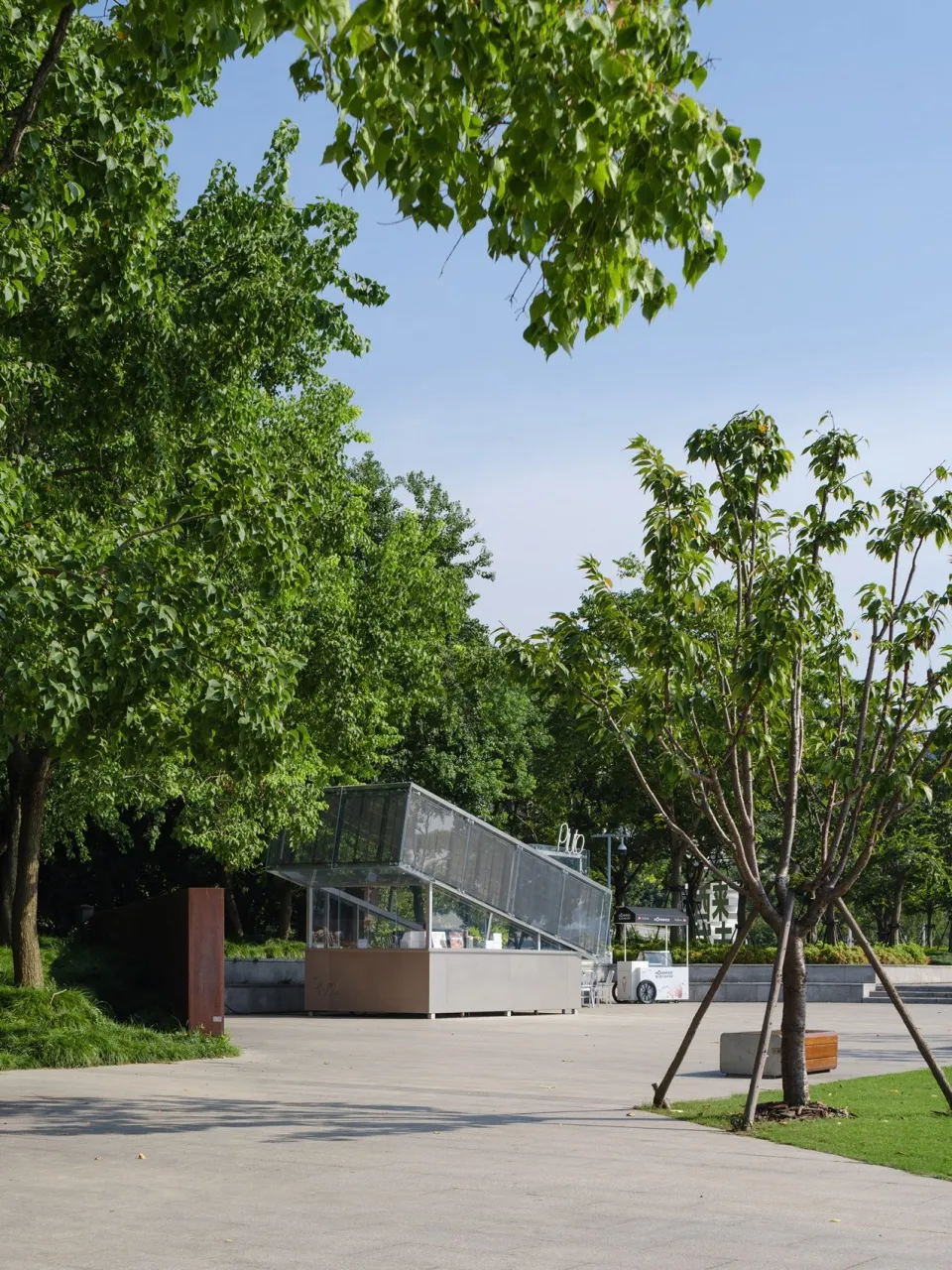 一座現代建築前方有大型玻璃結構，周圍環繞樹木，營造出公園或公共空間的氛圍