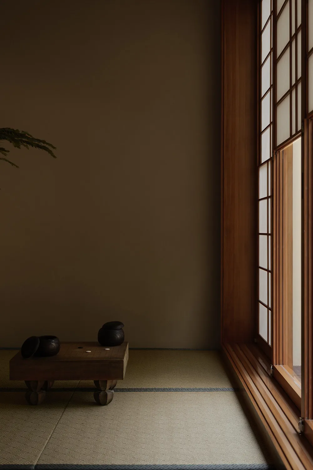 Cozy modern living area with a wooden floor, a large window, and two black bowls on a table, lit by natural sunlight