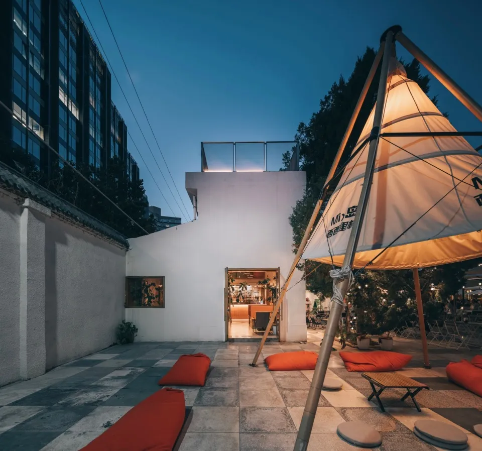 An outdoor dining area with a modern aesthetic, featuring a large umbrella, orange cushions, and a potted plant, set in a restaurant patio