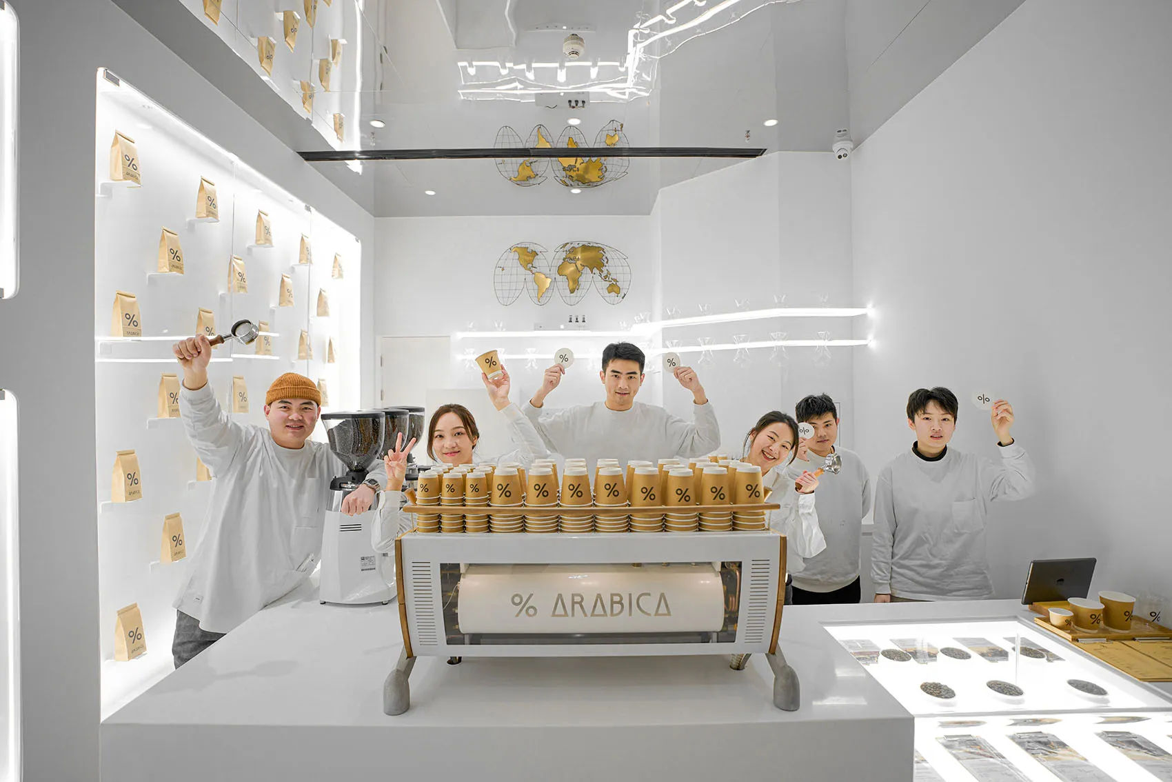 A group of people posing in front of an Arabica coffee machine with various canisters on display, creating a friendly and inviting atmosphere