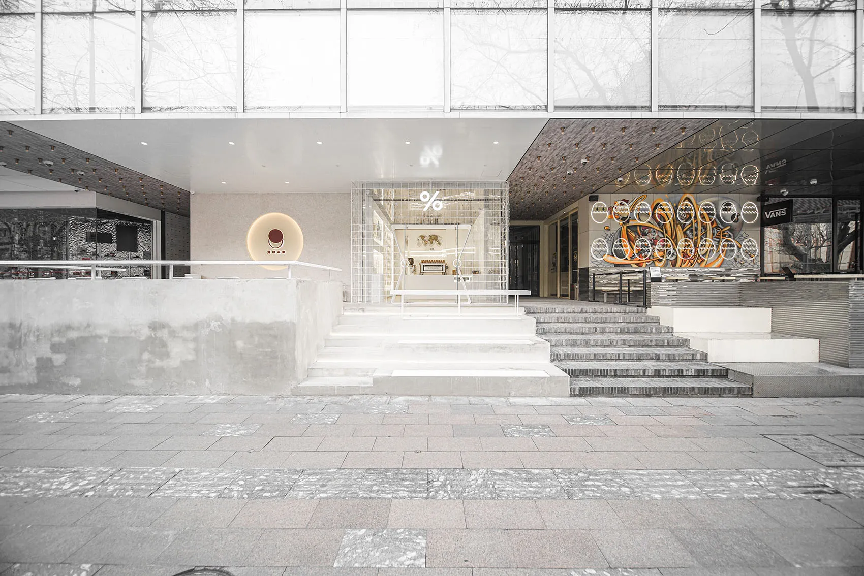 A modern commercial building with a large glass doorway, white frame, and two staircases leading upwards, giving off a sleek and modern vibe