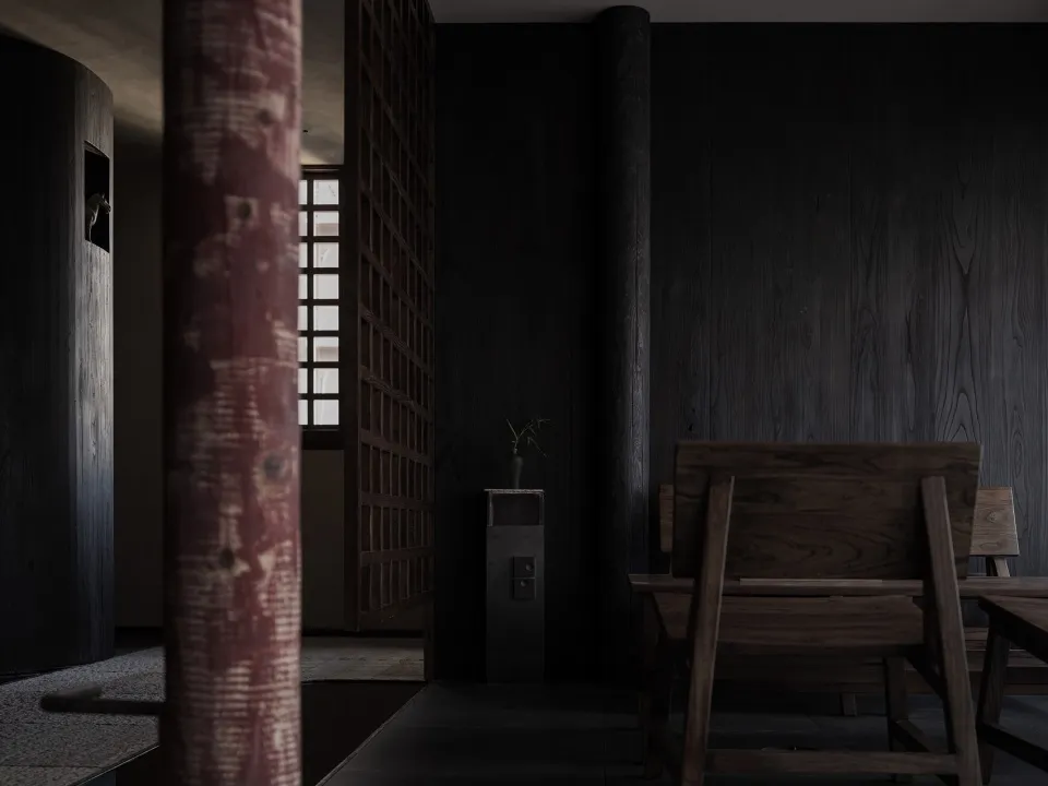 A dark dining space with a wooden table and chairs, surrounded by a black wall