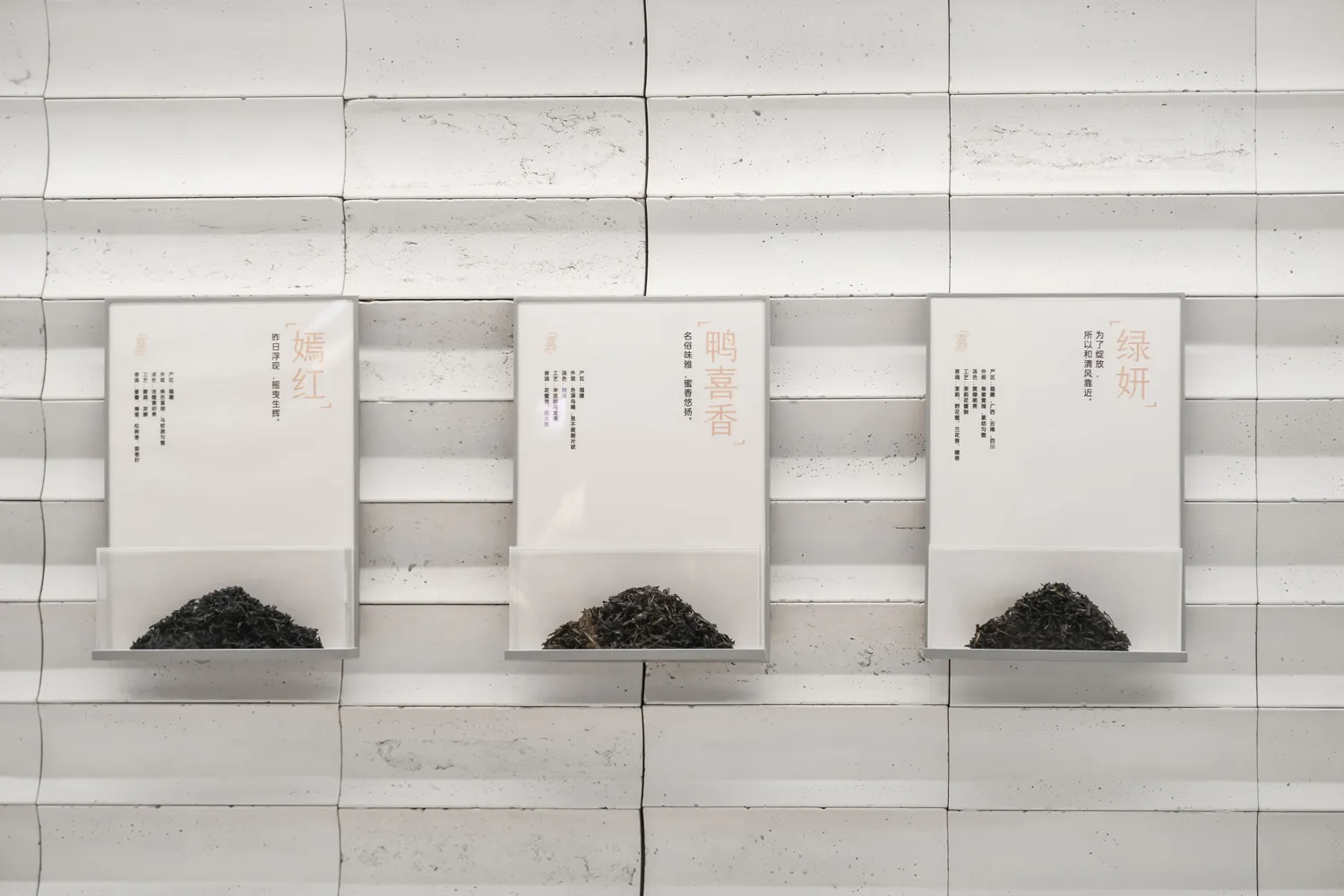 Three white boxes mounted on a wall, each containing small black objects, arranged in a row with one box above the other two