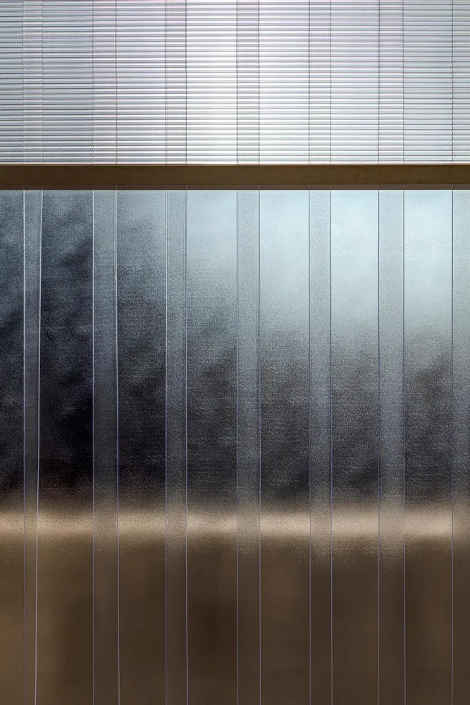 A large glass wall with a reflective metal surface, giving an industrial appearance in a minimalist setting