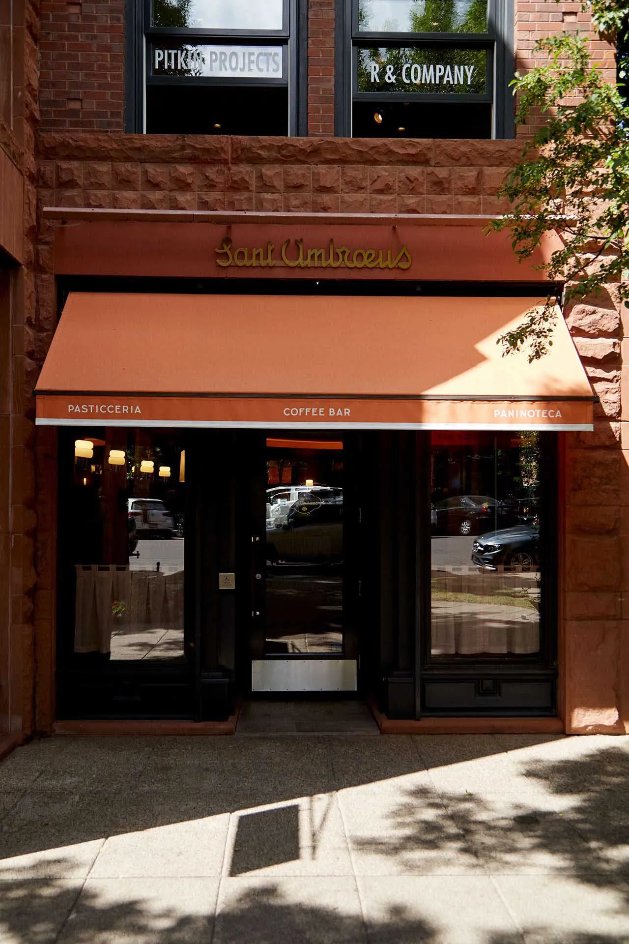 A charming cafe entrance with a brick facade, orange awning, and natural light from two windows on either side of the doorway