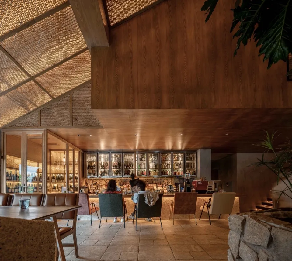 A social bar area with a dining table surrounded by chairs, bottles, and people enjoying a relaxed atmosphere