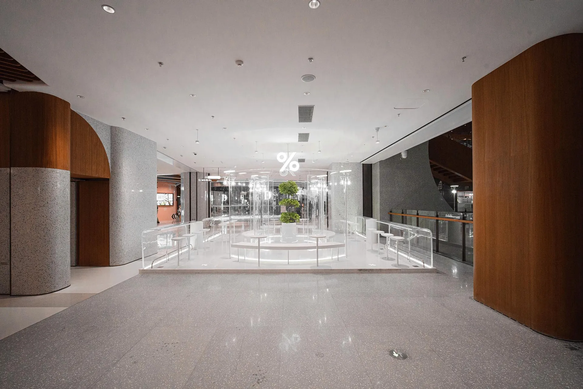 A modern lobby with a large circular table surrounded by chairs, potted plants, and natural light from windows