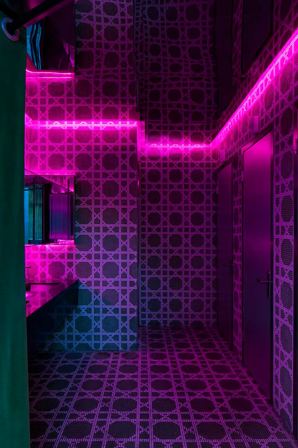 Bathroom with checkered patterned walls, pink and purple tiles, a sink, and a door
