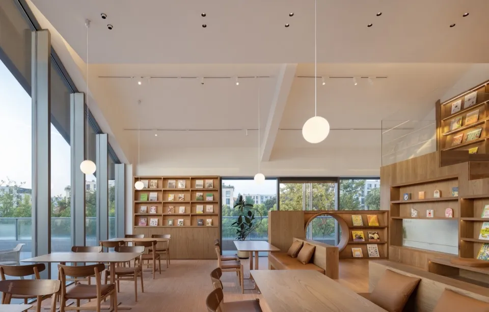 A calm and inviting study area with wooden floors and walls, featuring multiple tables and chairs, books, and potted plants