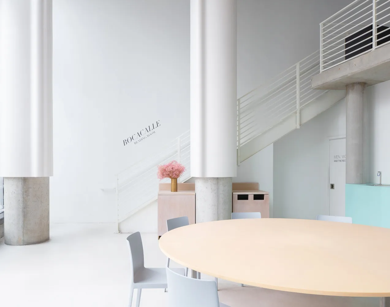 A calm and inviting lobby with a large wooden table and chairs, surrounded by a white room with no visible decorations or furniture beyond the table and chairs