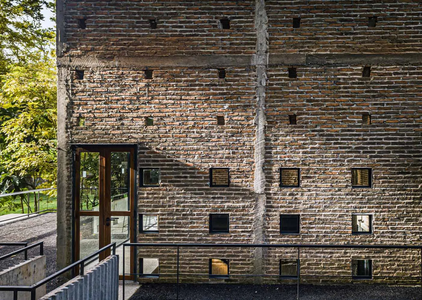 A traditional building with a brick wall and doorway, featuring windows on either side, with natural light and a sense of history