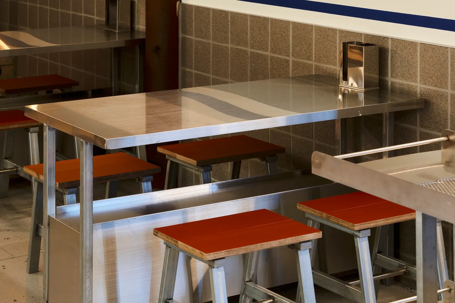 A modern restaurant interior with a large metal dining table surrounded by wooden chairs in a stylish and functional environment