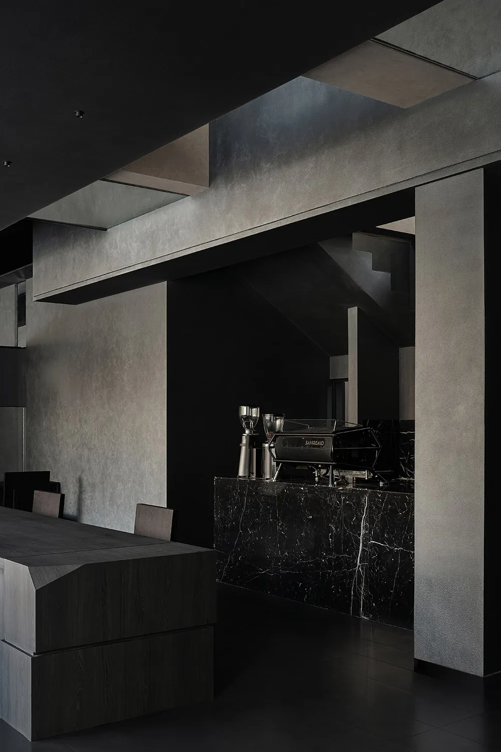 A dark and moody coffee shop interior with a black countertop, coffee machine, and cups, suggesting a nighttime setting