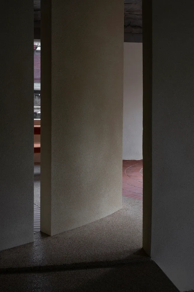 Narrow hallway with a red brick floor and white walls, featuring two archways and a dark atmosphere