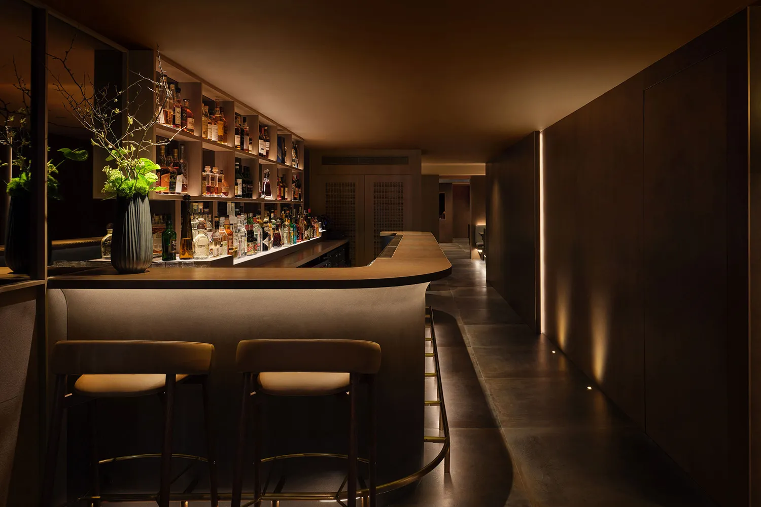 A sophisticated bar area with a long wooden counter, stools, and bottles of various sizes, creating an inviting atmosphere