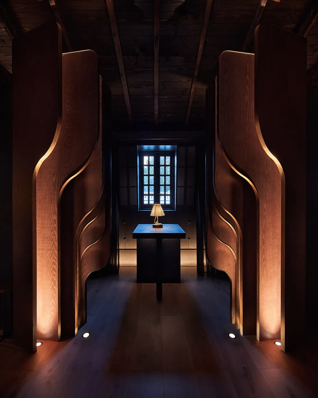 Warm and inviting interior space with wooden walls and floors, featuring a small lamp and large wooden doors