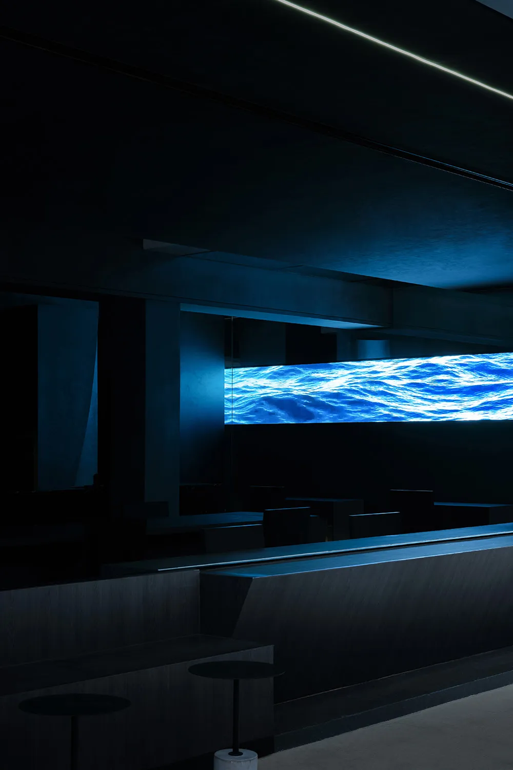 A darkened restaurant with a large blue waterfall as its centerpiece, surrounded by empty chairs and a sense of relaxation